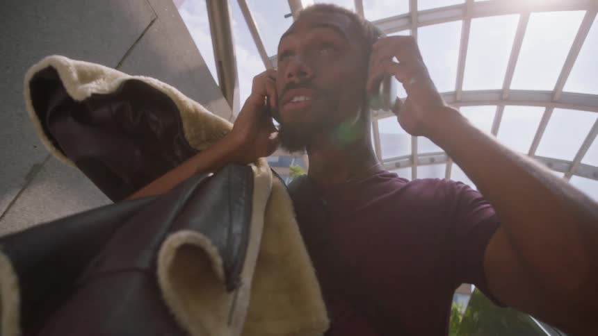 Man carrying a jacket puts on his headphones while riding the escalator downward under an arched glass ceiling