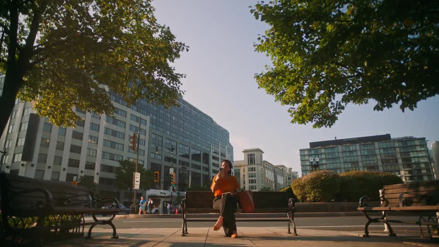 A woman looks at her smartphone while sitting on a bench in a city park