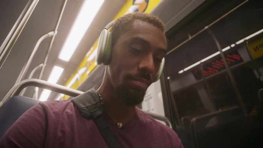 A young man sits inside a public transport vehicle wearing headphones and looking up