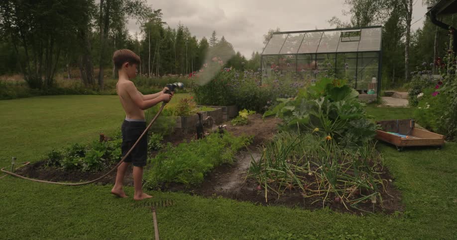 Boy in a garden holding a hose and spraying water on flowers