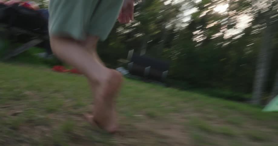 Barefoot boy runs across the grass on the shore on a cloudy day