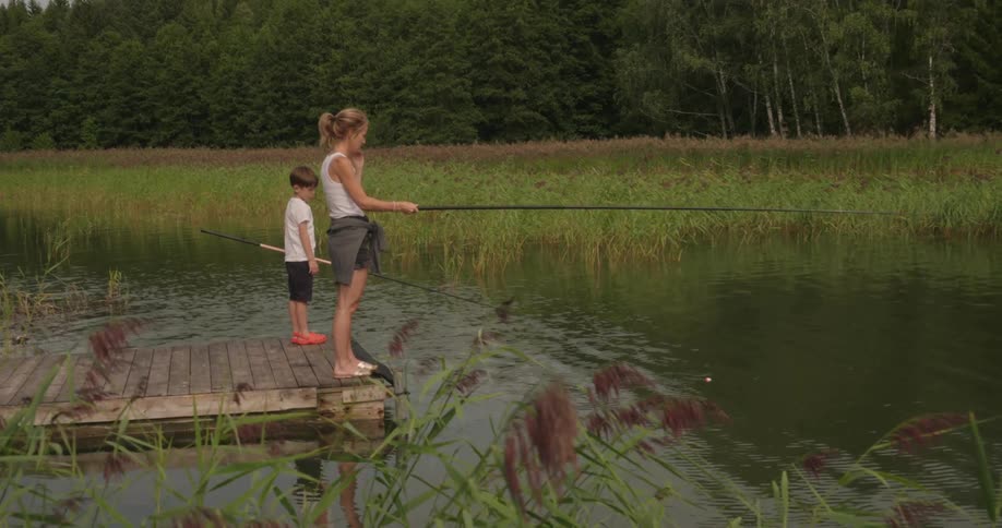 Mother and son stand on a wooden dock fishing on a calm lake