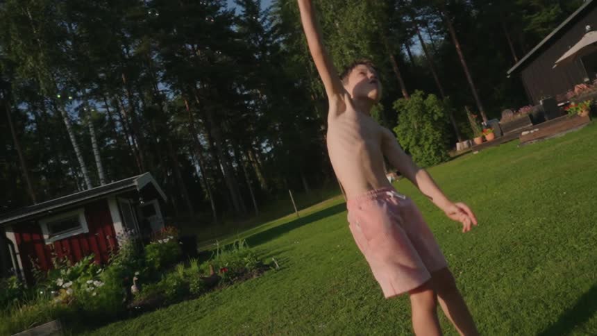 Topless boy wearing pink shorts jumps in the green backyard