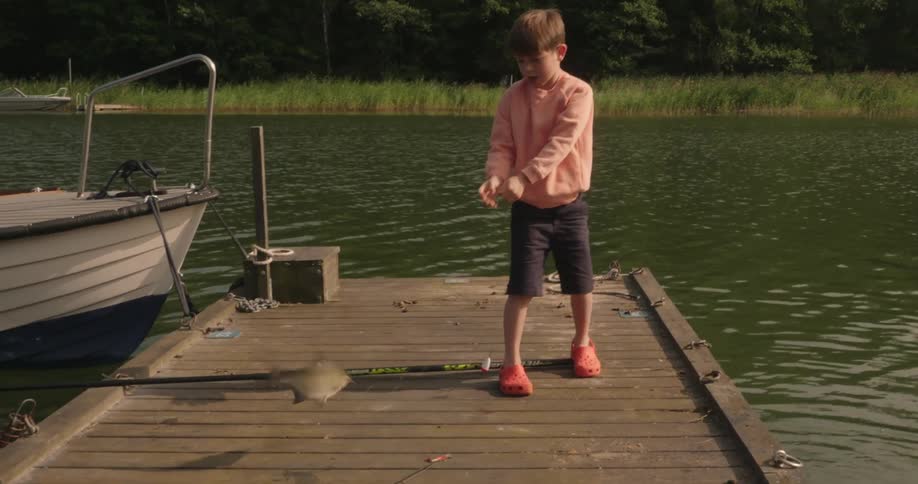 A young boy enjoys catching a fish in a lake and heckles the fish on a dock