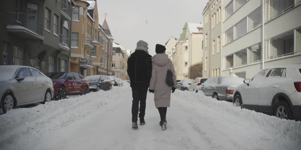 Man and woman holding hands walking down a snow covered street in a residential neighborhood