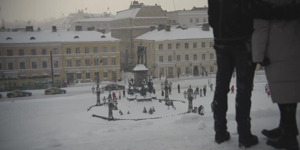 Man and woman seen from behind embracing enjoying the view of a square with a crowd of people on a snowy day