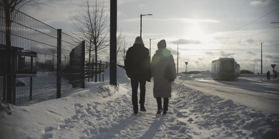 Back view of a couple holding hands walking through the city next to a train in a snowcovered environment
