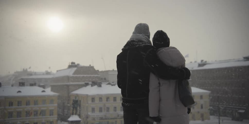 Couple on top of a hill overlooking a city square on a snowy day