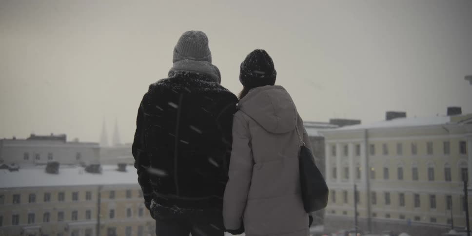 A couple hug each other on a winter landscape with a city in the background