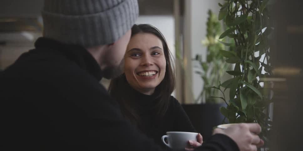 Man and woman holding cup of coffee talking happily to each other