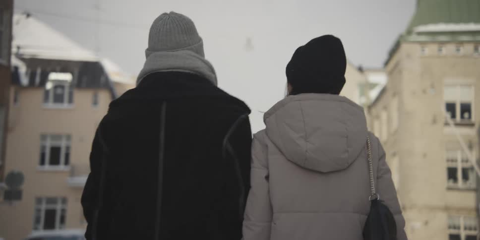 A man and a woman hold hands while walking through a snow covered city street