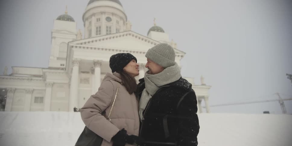 Couple consisting of a man and a woman taking a selfie and kissing in front of a palace on a snowy day
