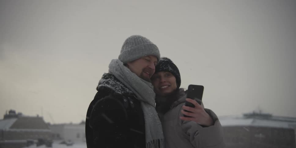 A couple takes a selfie kissing in the snow after they turn to look into the distance