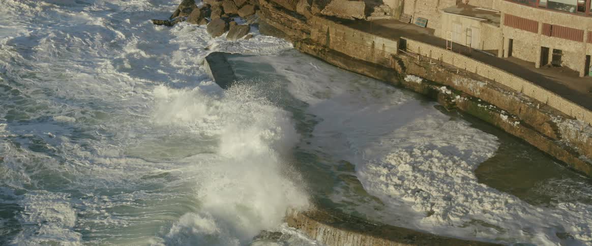 Strong ocean waves crashing against a rocky wall on the edge of the city