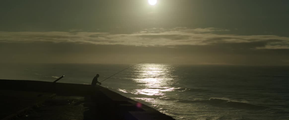Silhouette of a person fishing in a vast ocean with a sun on the horizon
