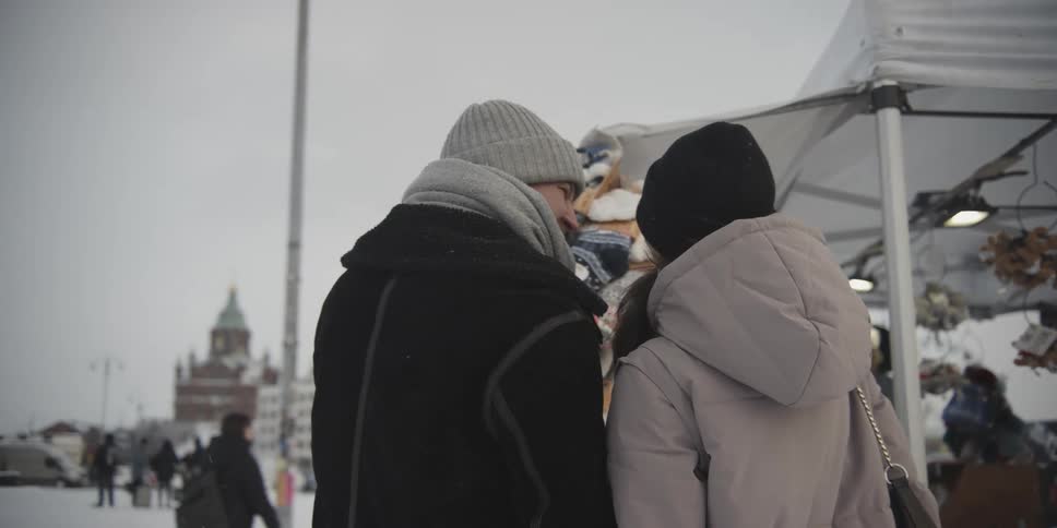 A couple look at products at an outdoor market while it snows in a city