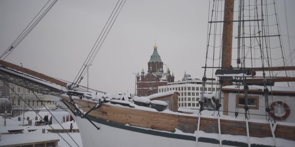 A wooden sailboat with snowcovered ropes is docked in a harbor