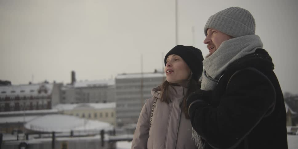 Couple standing side by side with the woman pointing as they talk on a snowy day
