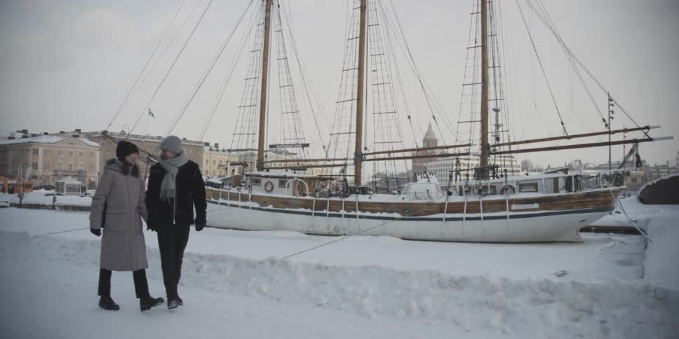 Woman and man walking side by side holding hands on a snow covered ground and on the edge of a sailing boat
