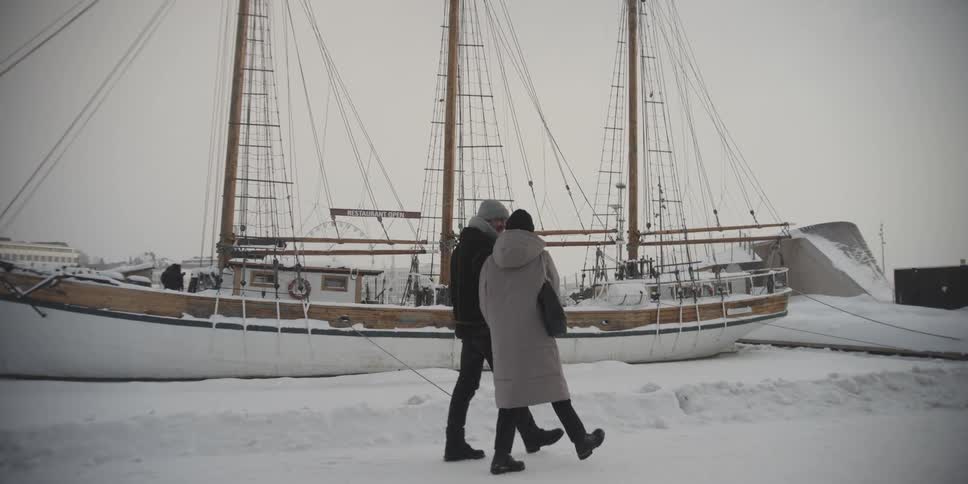 Couple walking hand in hand next to a sailboat moored on a snow covered ground