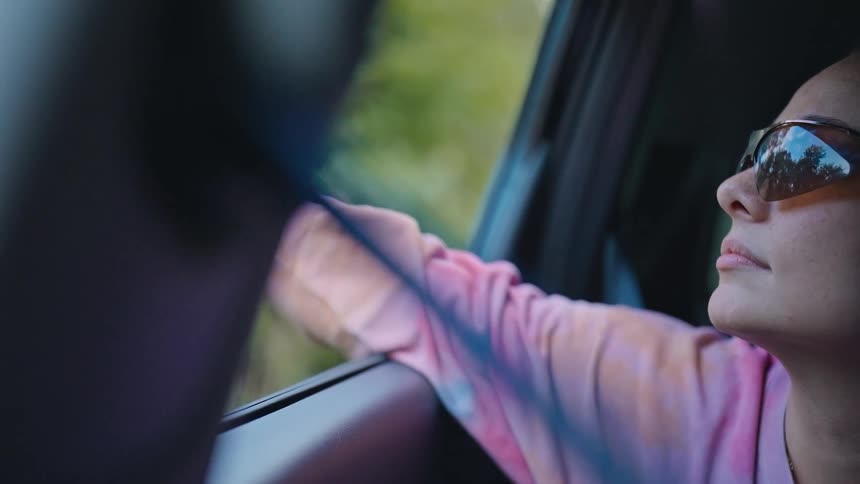 Woman with sunglasses and arms out of a moving car window