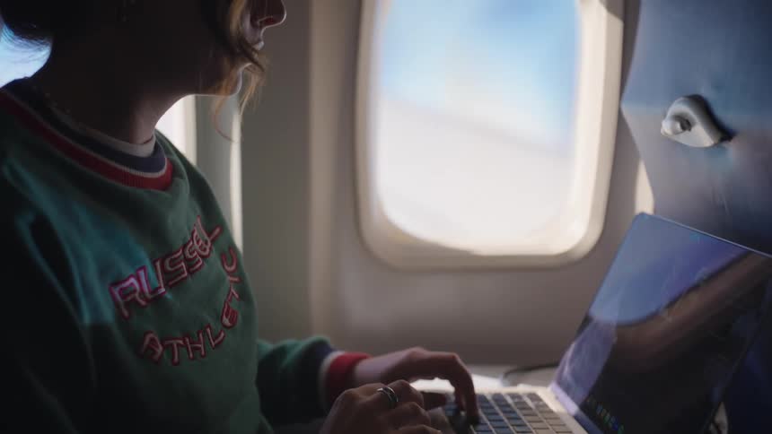 Woman sitting on an airplane seat midflight typing on a laptop