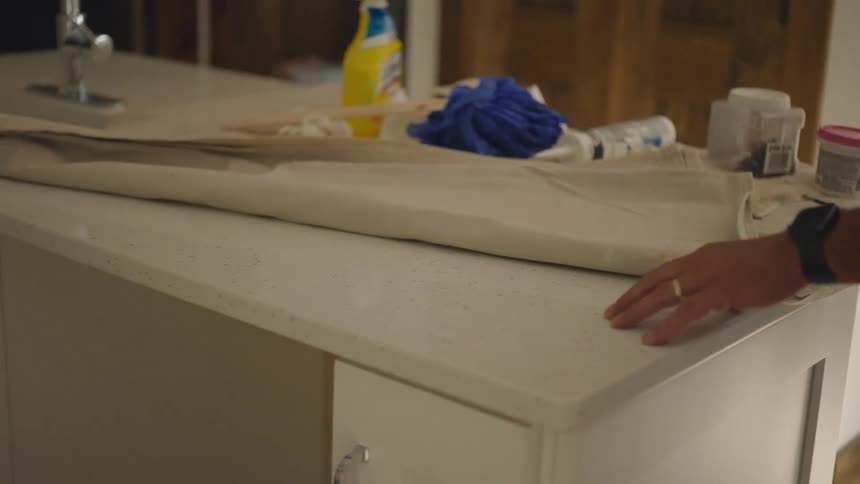 Closeup of a persons arm touching on a countertop next to a tarp and some tools