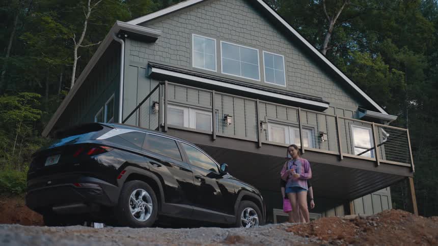 Two men and a woman walk toward a black car parked in front of a rural house