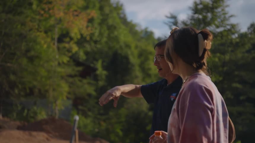 Man and woman talking while standing on a field with trees around