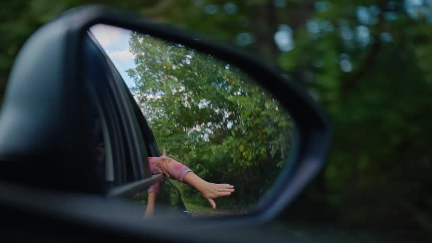 Rear view view of a moving car of a person with their hand out moving it through the air