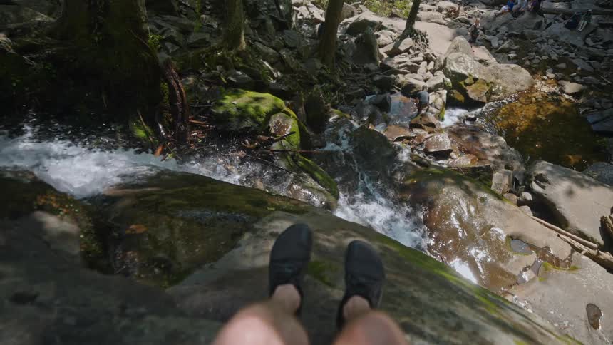 A male sits on top of a cliff next to a waterfall