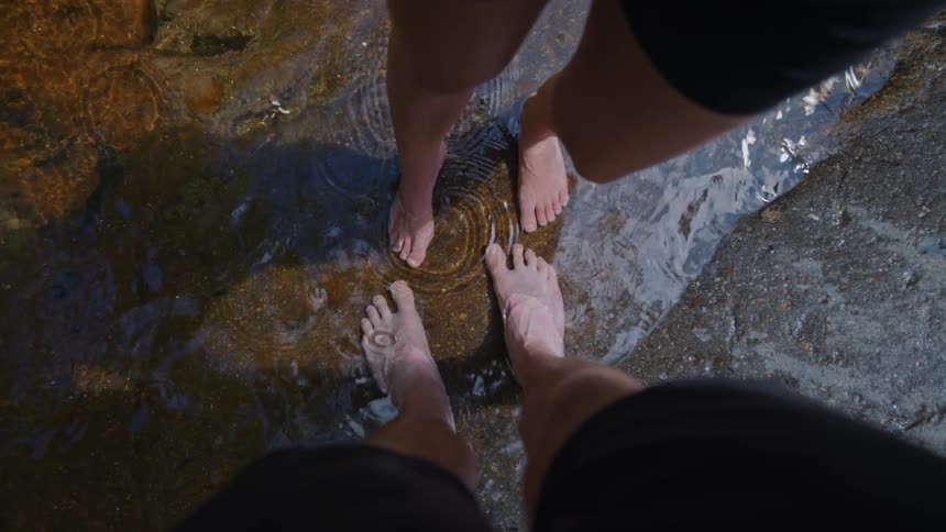 Two people with bare feet stand in shallow water
