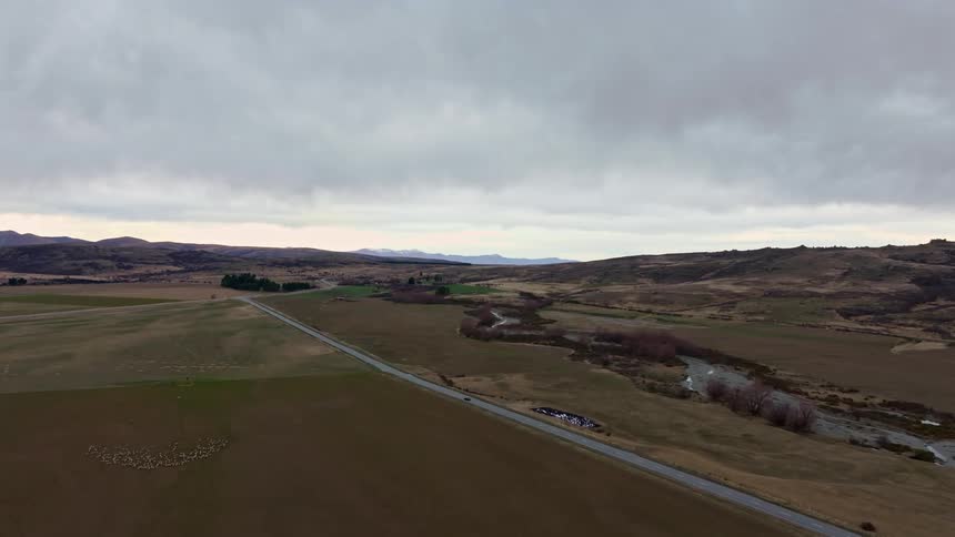 Aerial view of a highway passing through fields with mountains around on a cloudy day