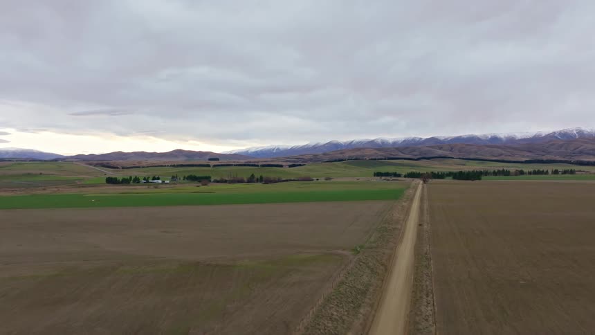 Across a straight dirt road aerial of agricultural land on a cloudy day