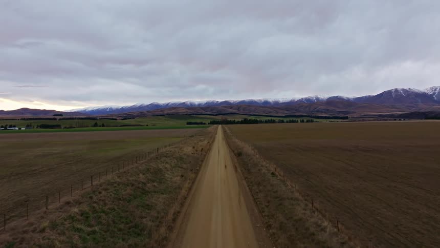Low level tracking down a straight dirt road the landscape leads to a mountain range