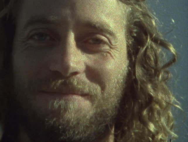 Closeup of a blonde man with curly hair and a beard captured on vintage film