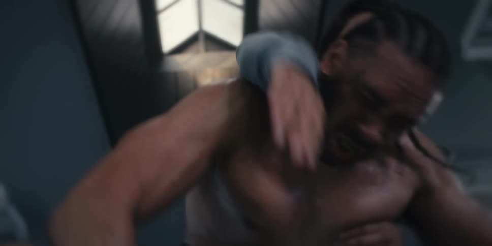 A man with black gloves and no shirt is punching the ground and then some men restrain him