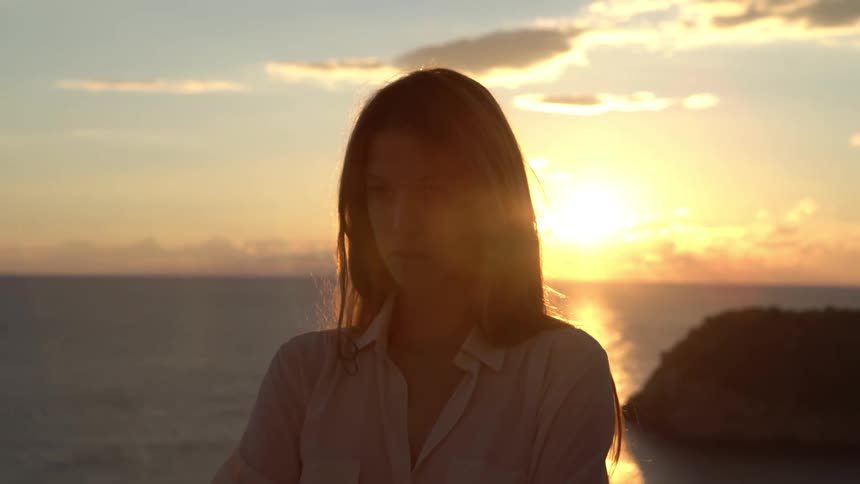 Silhouette of a blonde woman with long hair standing by the ocean at sunset