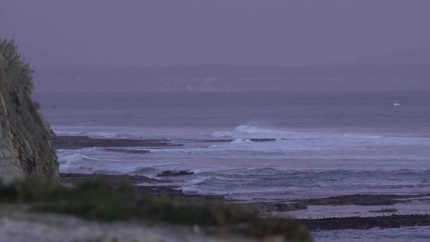 Landscape of a beach with waves against a purple sky