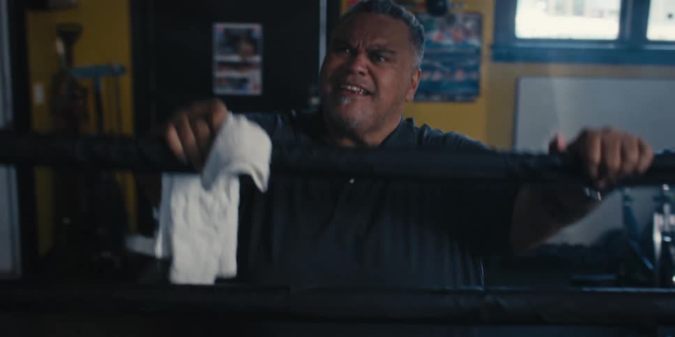 Older man holding on to the boxing ring rope at a gym throws down a towel
