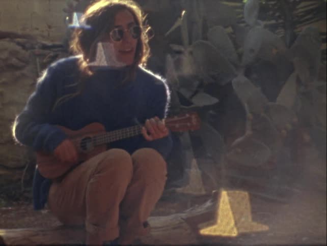 Individual seated outdoors playing a guitar captured on vintage film