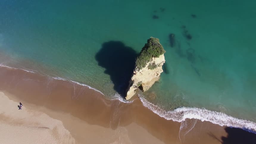 Aerial view of person walking on a beach with clear turquoise waters and a large promontory