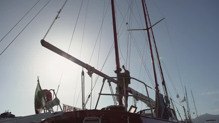 A young man threading rope on the mast of a sailboat under a clear blue sky