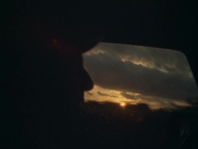 Silhouette of a person against a car window with a sunset sky in the background