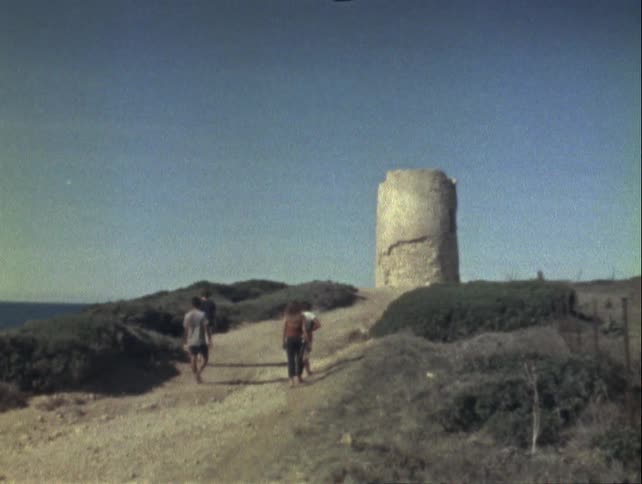 Group of four people walking towards a cylindrical tower on a hill