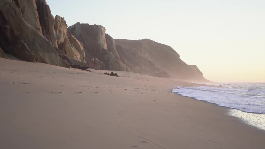 Landscape of sea waves reaching the sand next to the rocky coast one morning