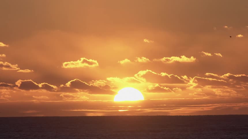 Sunset with the sun partially obscured by clouds near the horizon over a calm sea
