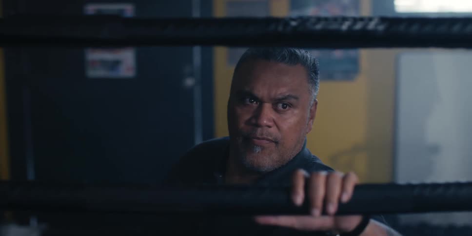 Closeup of a boxing coach standing next to a boxing ring watching a fight inside the ring