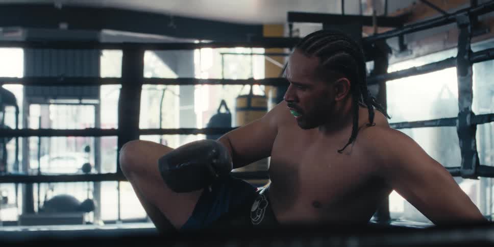 Man lying on the floor of a ring looking at his boxing gloves