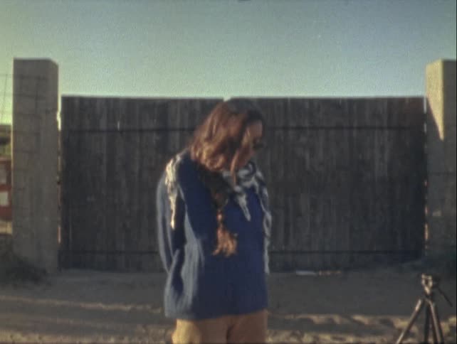Woman standing in front of a large gate with concrete posts on either side